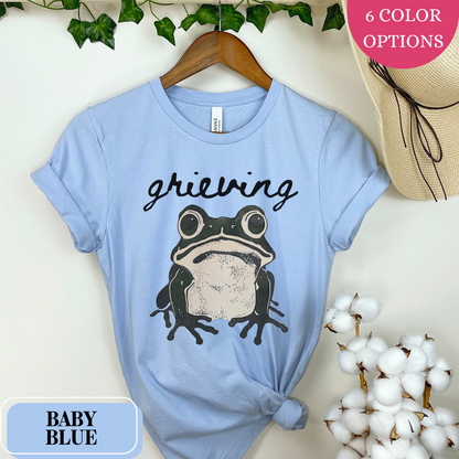 Baby Blue Bella Canvas 3001 T-shirt with a large frog graphic that says "Grieving". A way for people struggling with loss to convey their sorrow - makes a perfect gift for a friend or loved one struggling with grief.