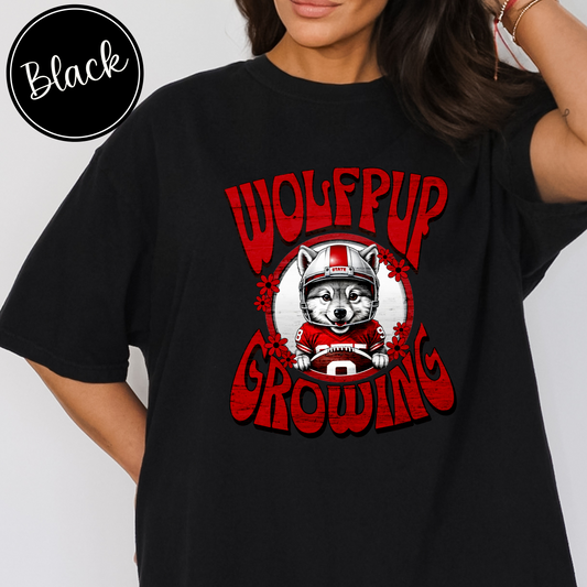 Black Comfort Colors t-shirt with an adorable wolf pup in a football helmet and jersey with the saying Wolfpup Growing, oversized shirt perfect for early maternity top for a NC state sports fan and mom-to-be.