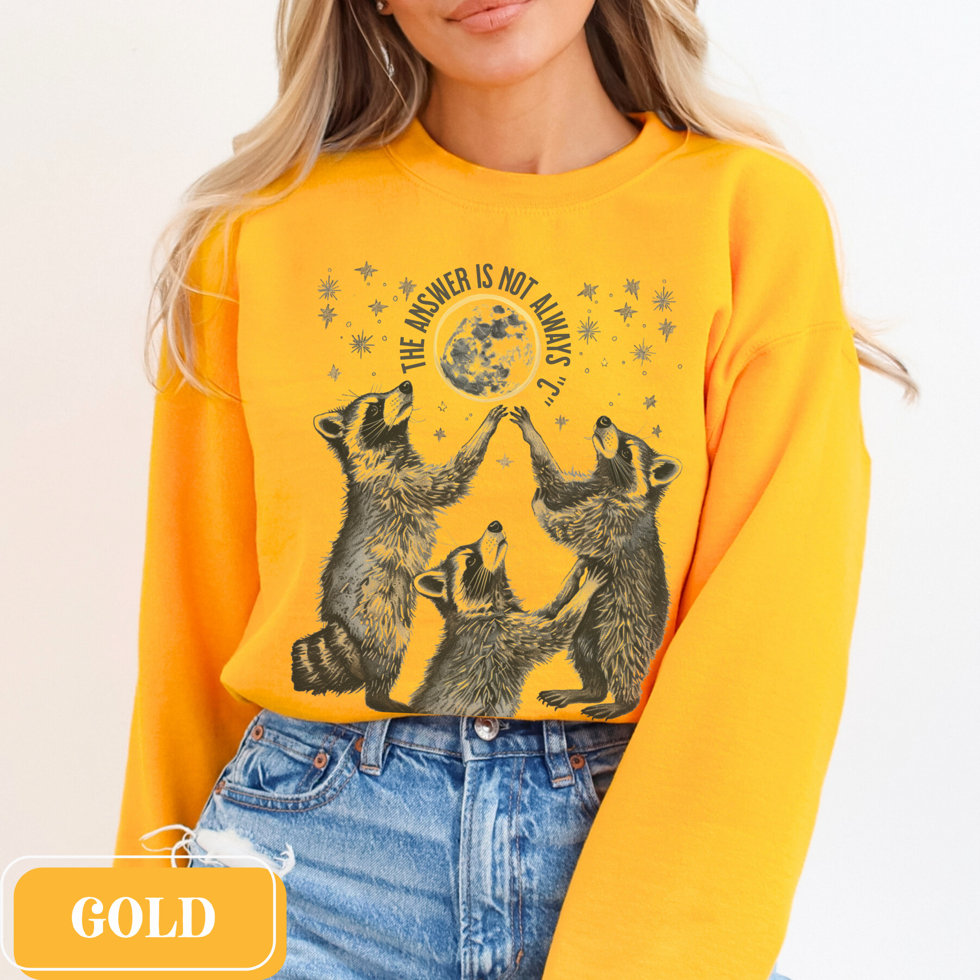 Gold Gildan 18000 Sweatshirt with large raccoon and moon/stars graphic that says "The Answer Is Not Always 'C'" - funny meme crewneck for teachers. Great gift for education grad or major, new teacher, educators, etc. Weird teachers goblincore.