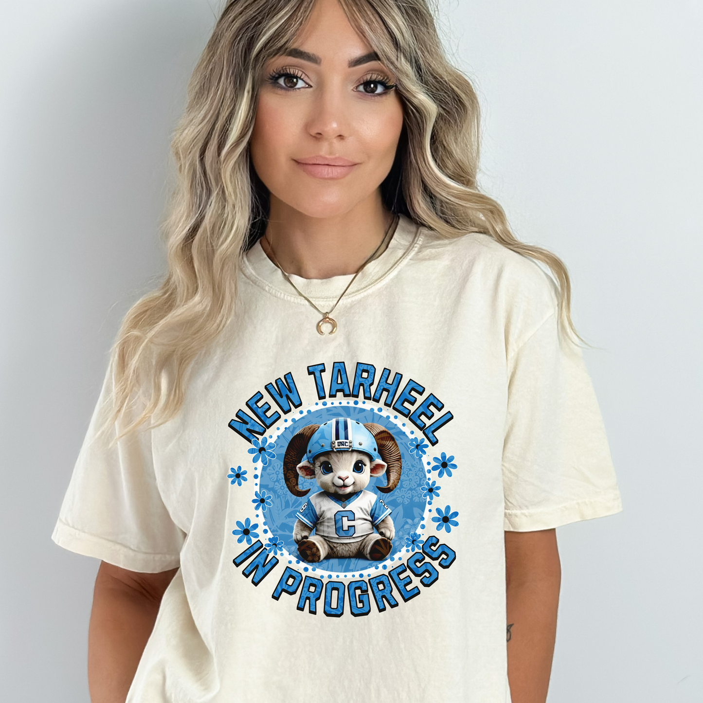 Ivory Comfort Colors t-shirt for tarheel fans and mother-to-be. These oversized tees are perfect for early maternity life, and show your love for Carolina sports. It features an adorable baby ram in a football helmet and jersey with the words New Tarheel In Progress.