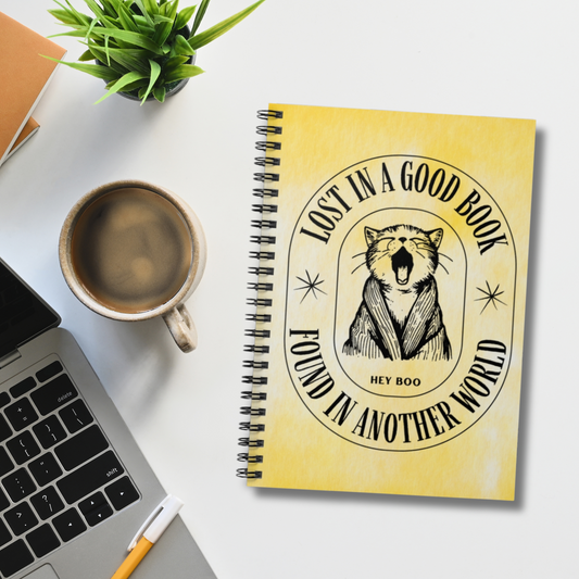 Tie dye yellow spiral notebook that says "Lost In A Good Book, Found In Another World". It has an adorable cat yawning graphic and makes the perfect gift for avid readers, book lovers, English majors, Teachers, and librarians.