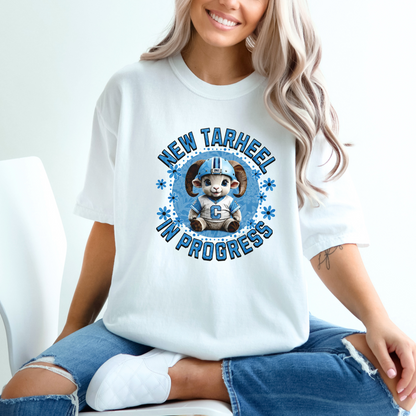 White Comfort Colors t-shirt for tarheel fans and mother-to-be. These oversized tees are perfect for early maternity life, and show your love for Carolina sports. It features an adorable baby ram in a football helmet and jersey with the words New Tarheel In Progress.