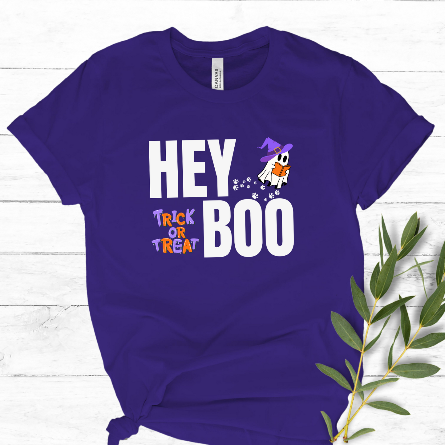 Purple Bella Canvas Hey Boo Halloween t-shirt with an adorable ghost reading with a witches hat on, and paw prints leading up to it. Trick or Treat.