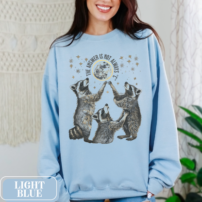 Light Blue Gildan 18000 Sweatshirt with large raccoon and moon/stars graphic that says "The Answer Is Not Always 'C'" - funny meme crewneck for teachers. Great gift for education grad or major, new teacher, educators, etc. Weird teachers goblincore.