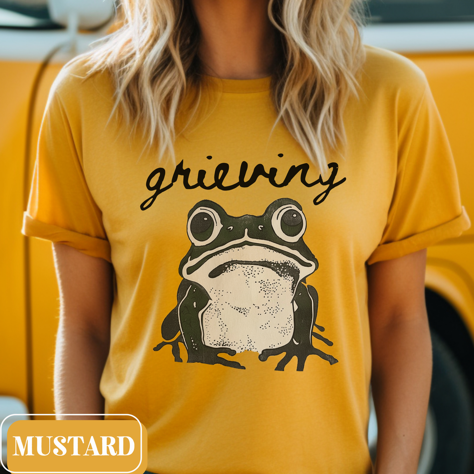 Mustard Bella Canvas 3001 T-shirt with a large frog graphic that says "Grieving". A way for people struggling with loss to convey their sorrow - makes a perfect gift for a friend or loved one struggling with grief.