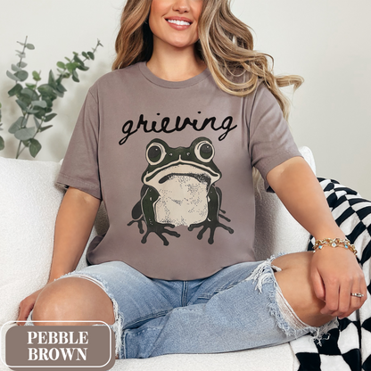 Pebble Brown Bella Canvas 3001 T-shirt with a large frog graphic that says "Grieving". A way for people struggling with loss to convey their sorrow - makes a perfect gift for a friend or loved one struggling with grief.